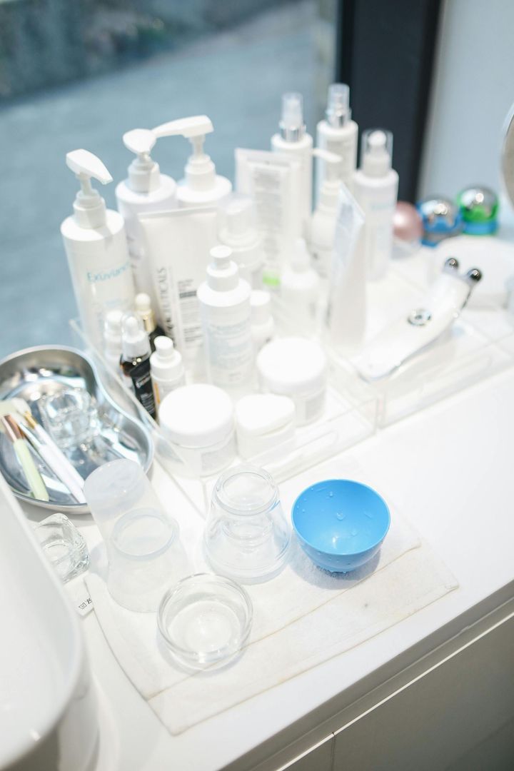 Skincare products and tools on a white counter: bottles, jars, mixing bowls, and a metal tray.