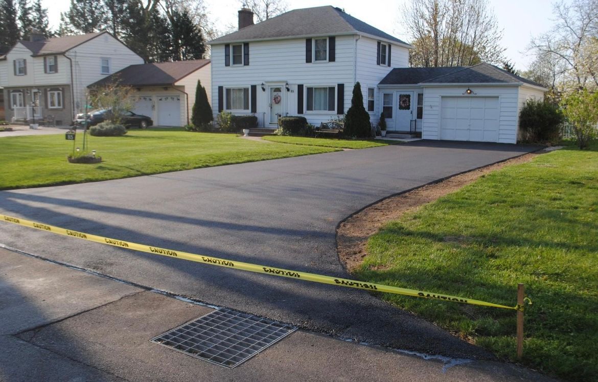 Asphalt driveway paving process in action by Universal Paving & Concrete in Rochester, NY, with professional equipment ensuring a perfect finish.