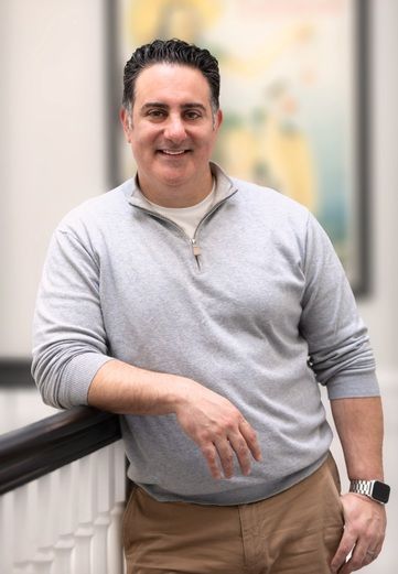 A man in a grey sweater and khaki pants is leaning on a railing.
