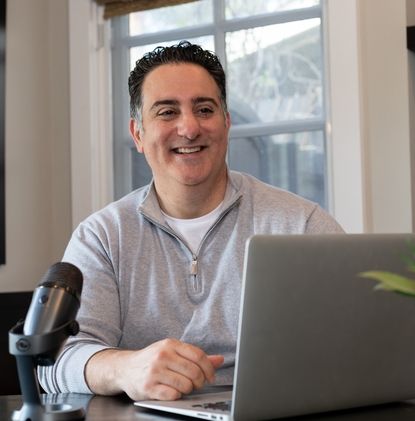A man is sitting at a table with a laptop and a microphone.