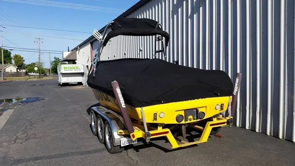 A yellow boat with a black cover is parked in front of a building