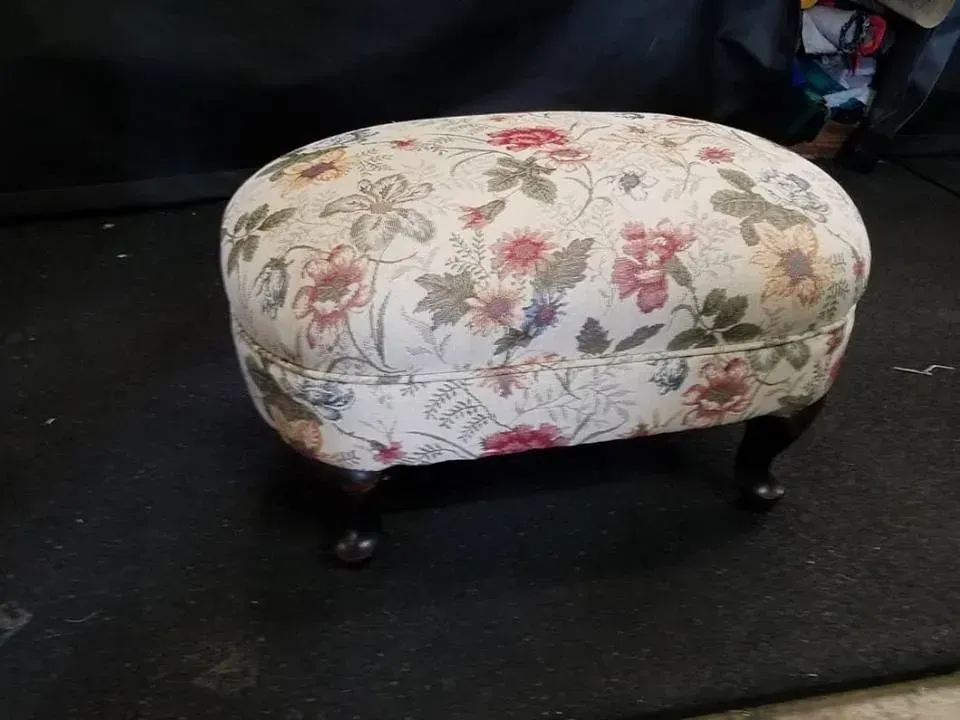 A floral ottoman is sitting on a black mat.