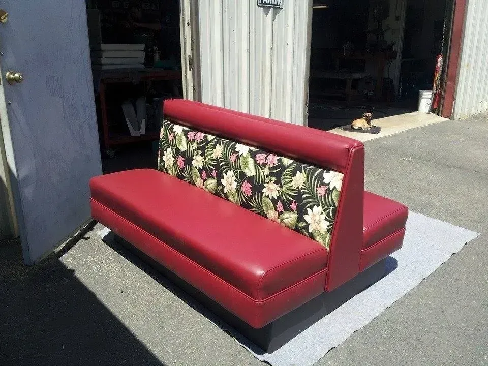 A red couch with a floral backrest is sitting in front of a building.