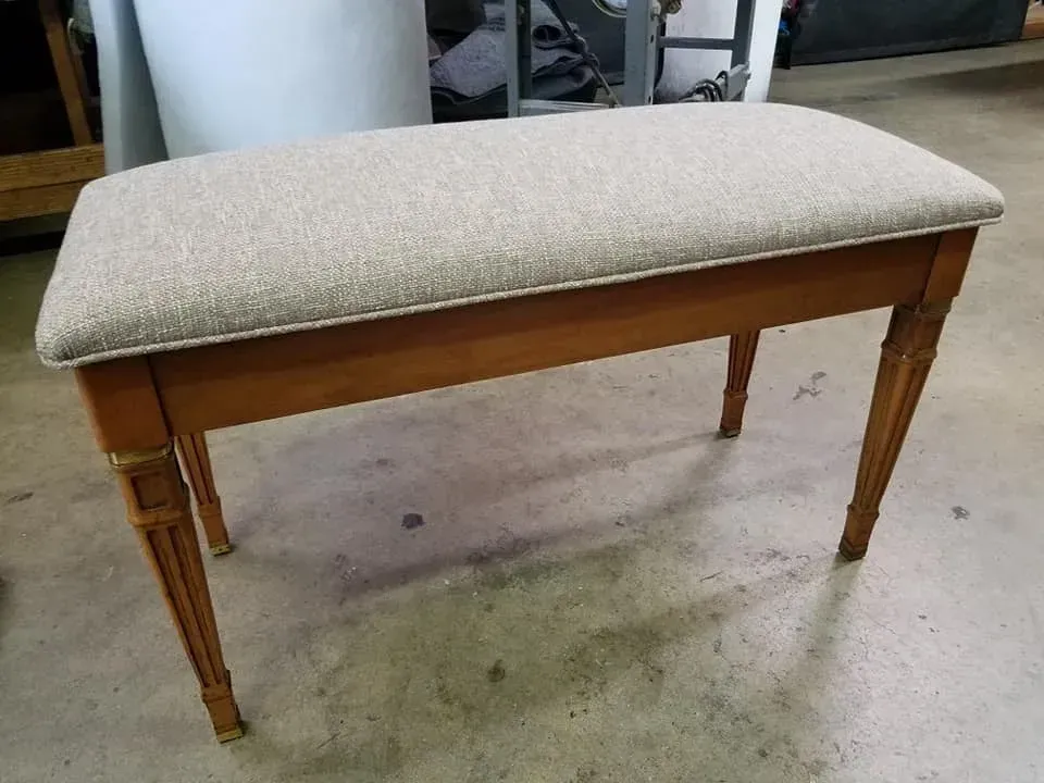 A wooden bench with a beige cushion is sitting on a concrete floor.