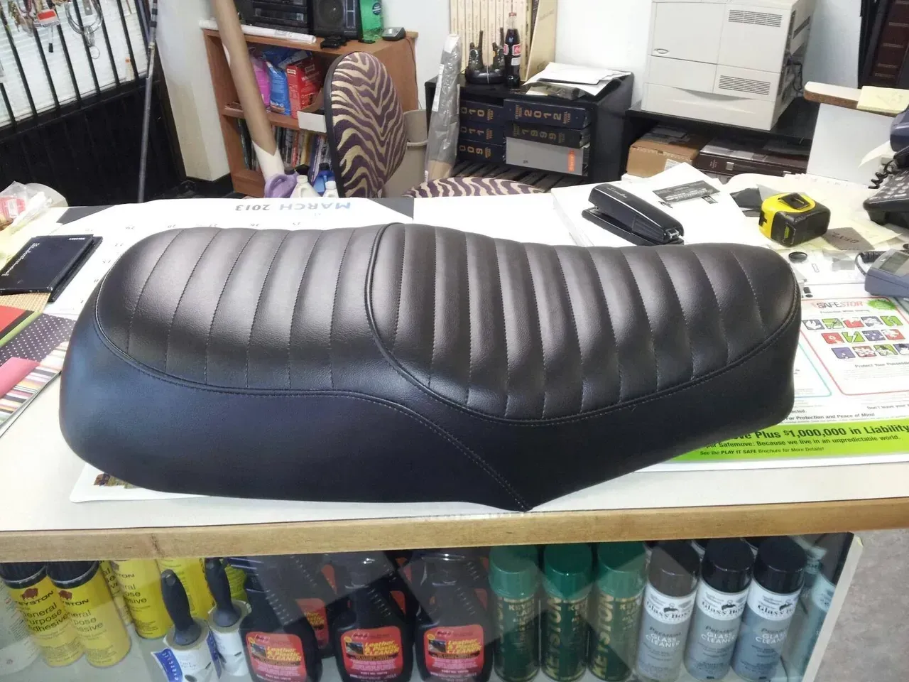 A black motorcycle seat is sitting on a wooden table
