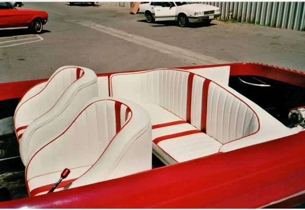A red boat with white seats is parked in a parking lot
