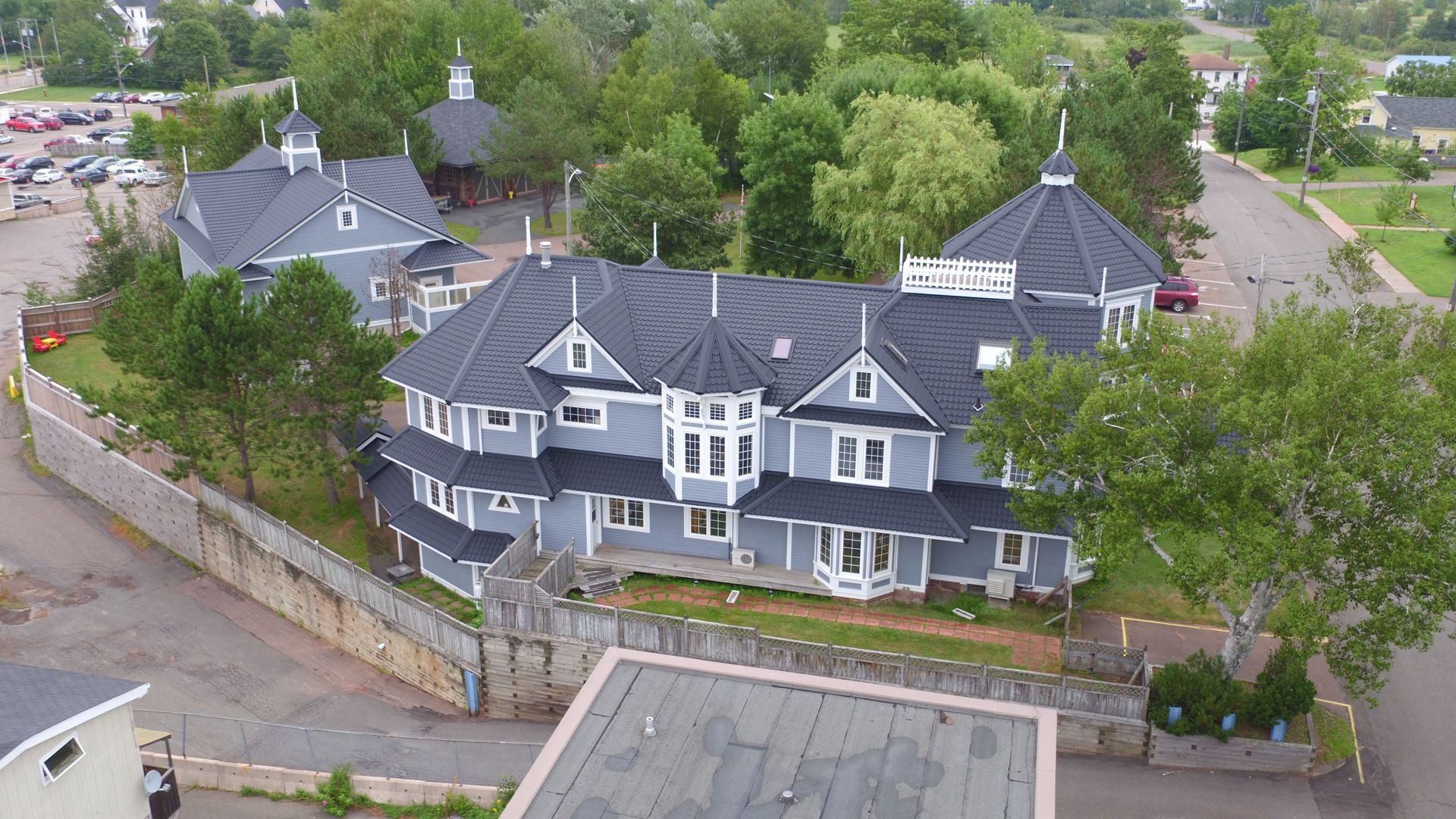 Gray Victorian house with dark roof, surrounded by trees and a stone wall.