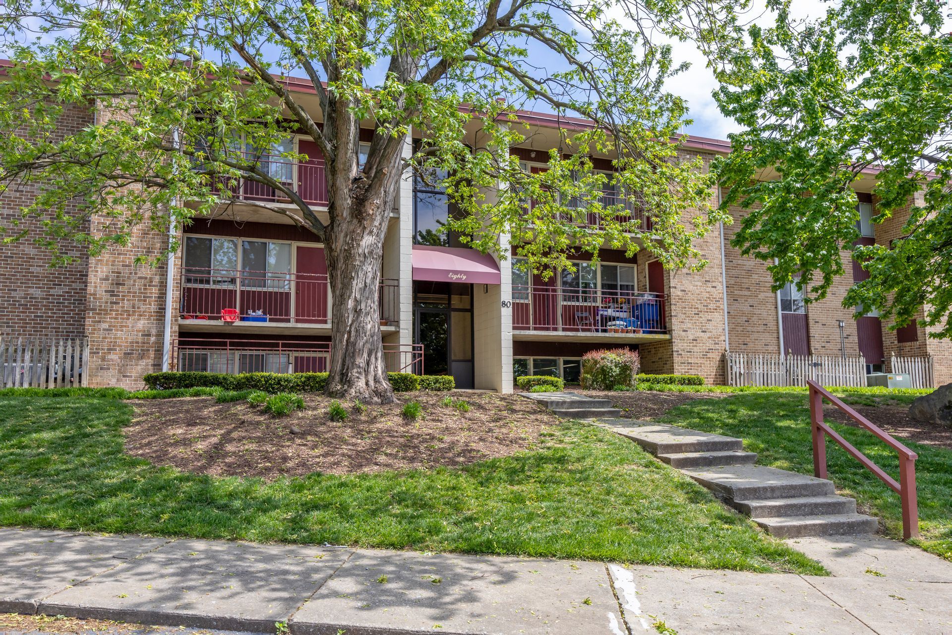 A large apartment building with stairs leading up to it and a tree in front of it.