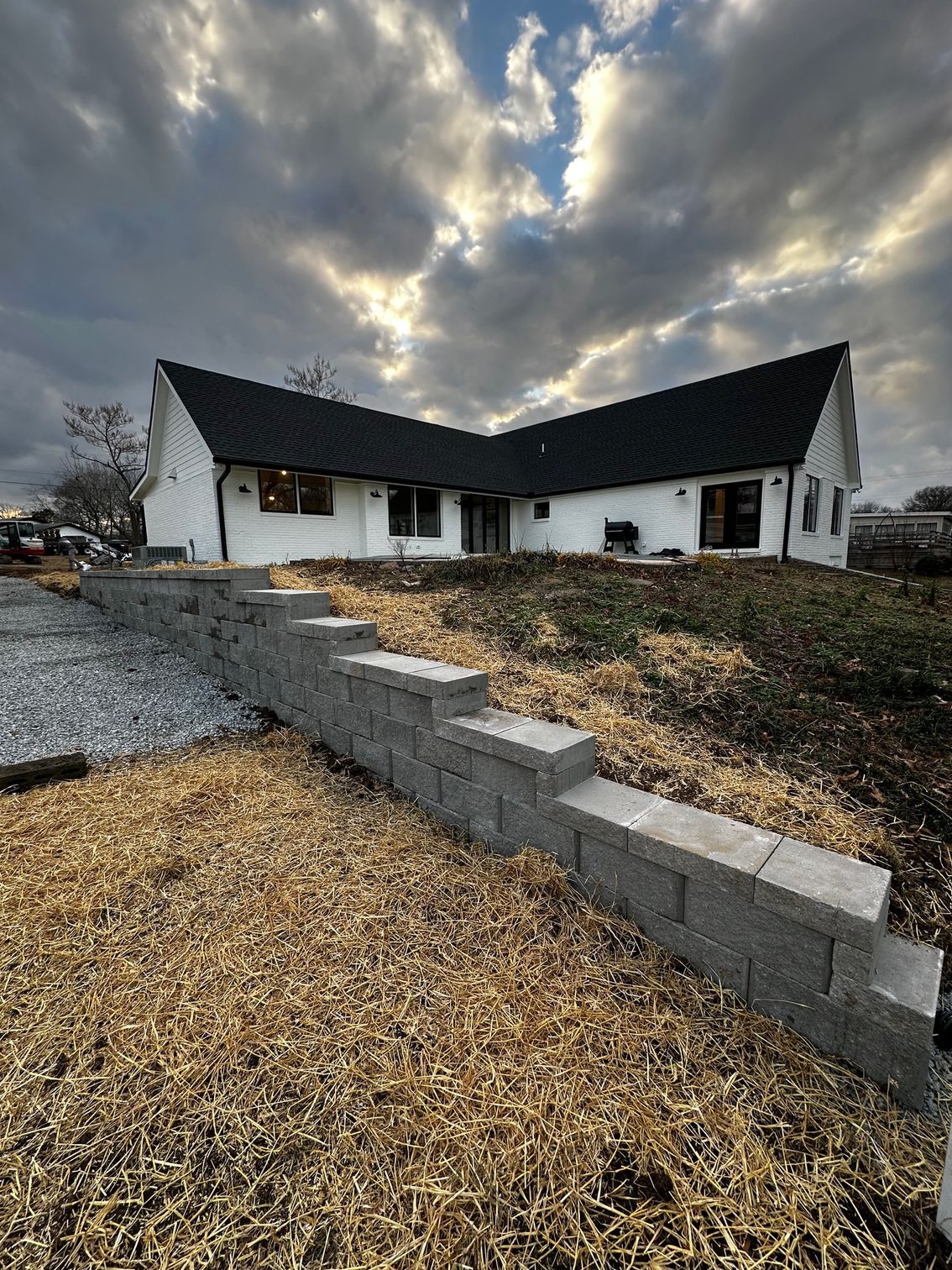 A white house with a black roof and a brick wall in front of it.