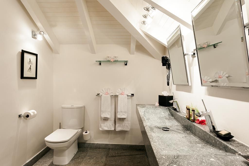White bathroom with sloped ceiling, stone sink, toilet, and two hanging mirrors.