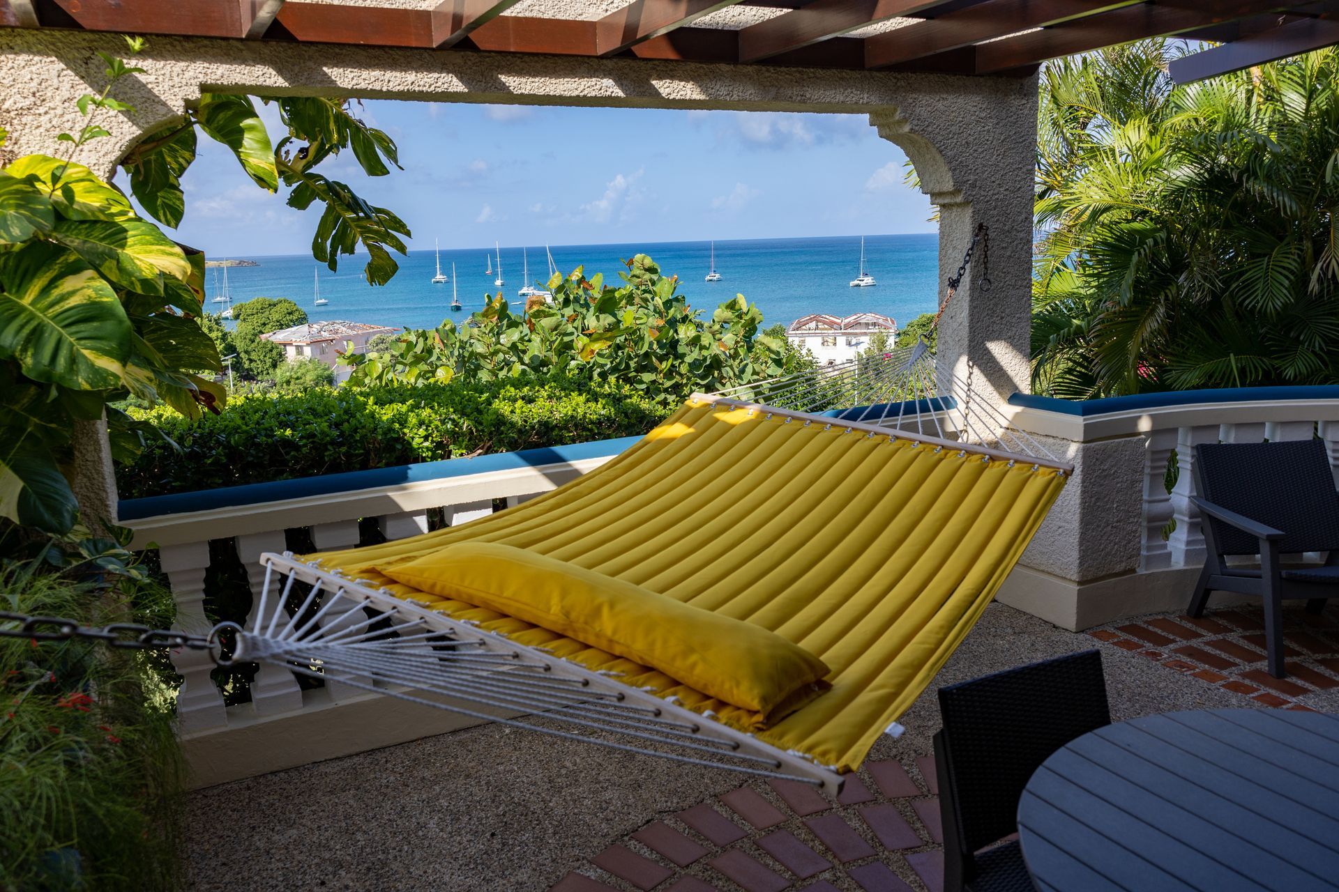 Yellow hammock on a patio overlooking a blue ocean with sailboats.