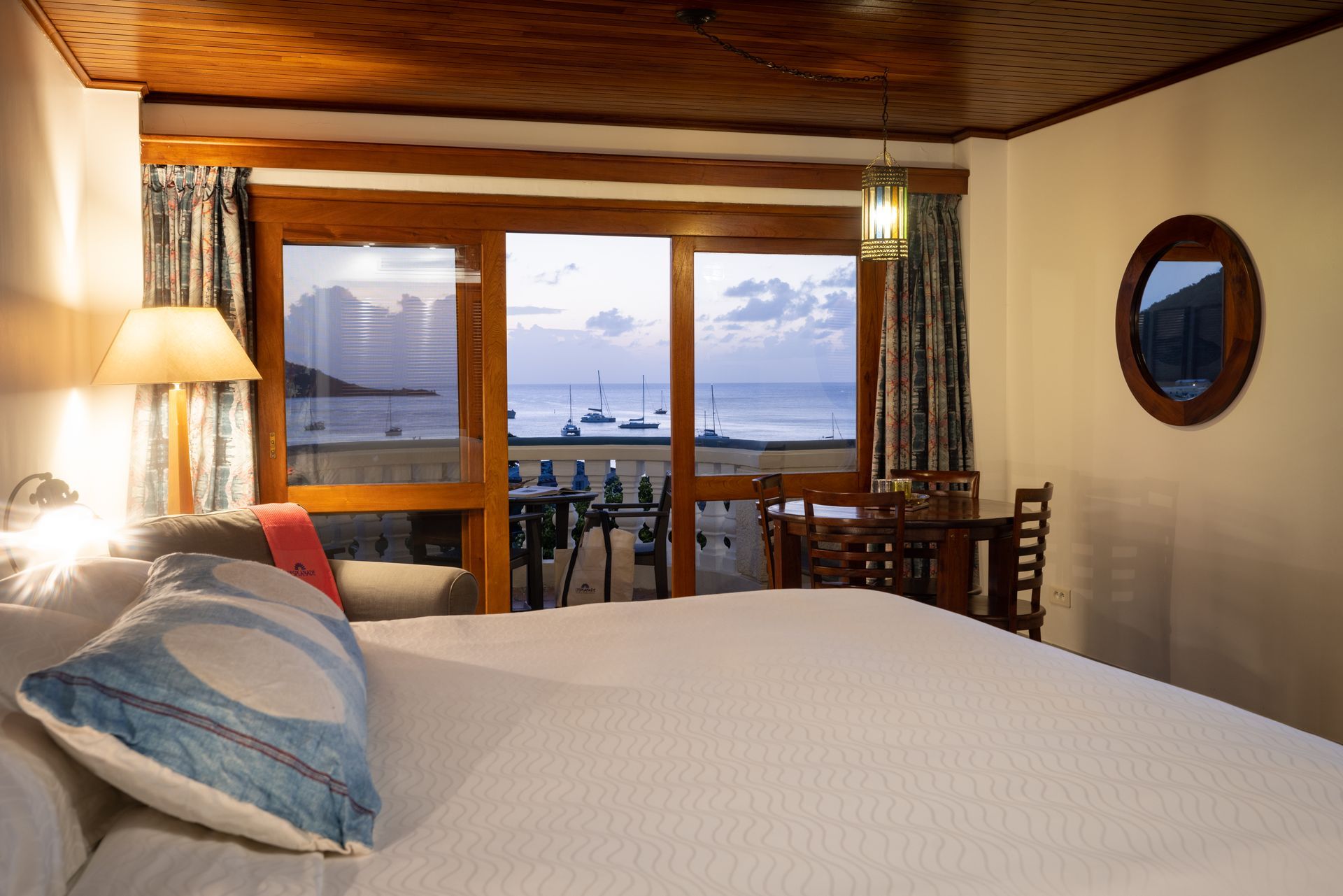 Bedroom with bed, water view through open doors, wooden ceiling and trim.