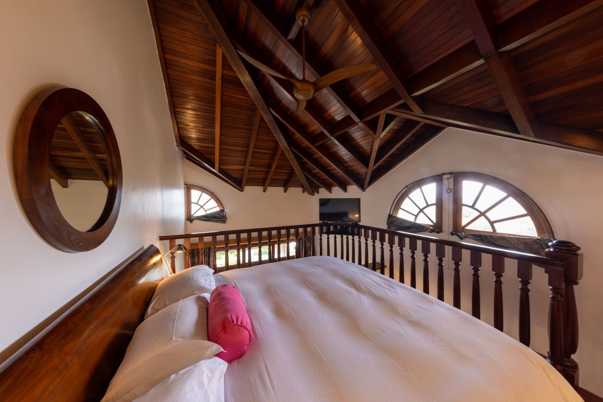 Loft bedroom with a large bed, arched windows, and exposed wooden beams.