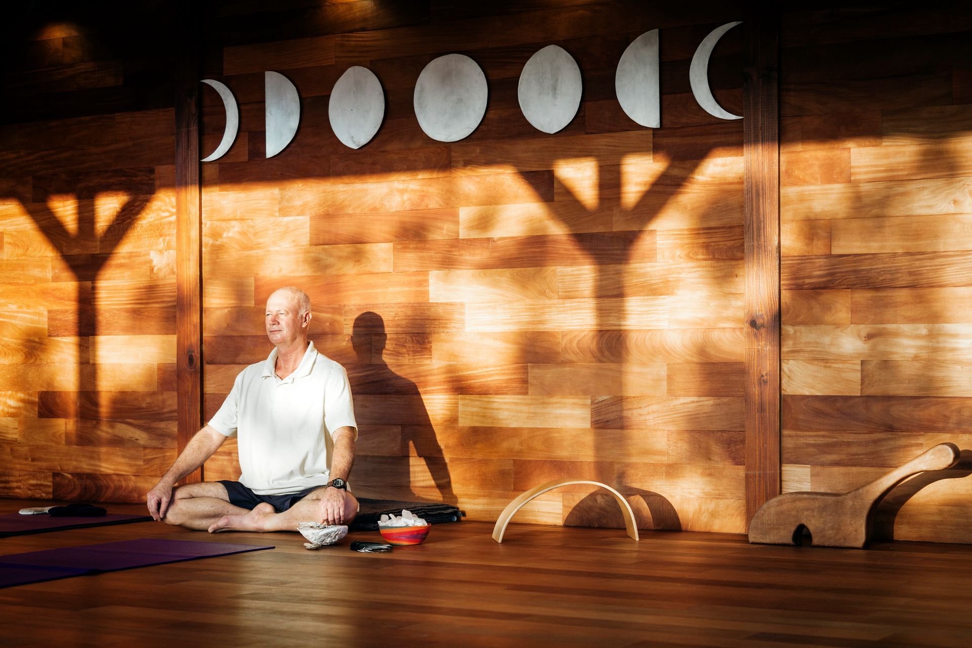 Man meditating in yoga studio with wood paneling and moon phase decor.