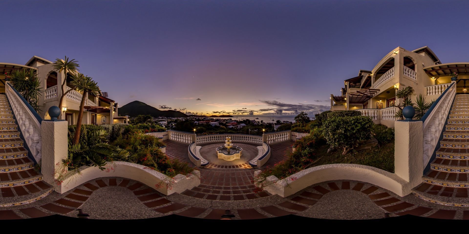 Night view of a luxury resort overlooking the ocean, with white buildings, brick steps, and a colorful sunset sky.