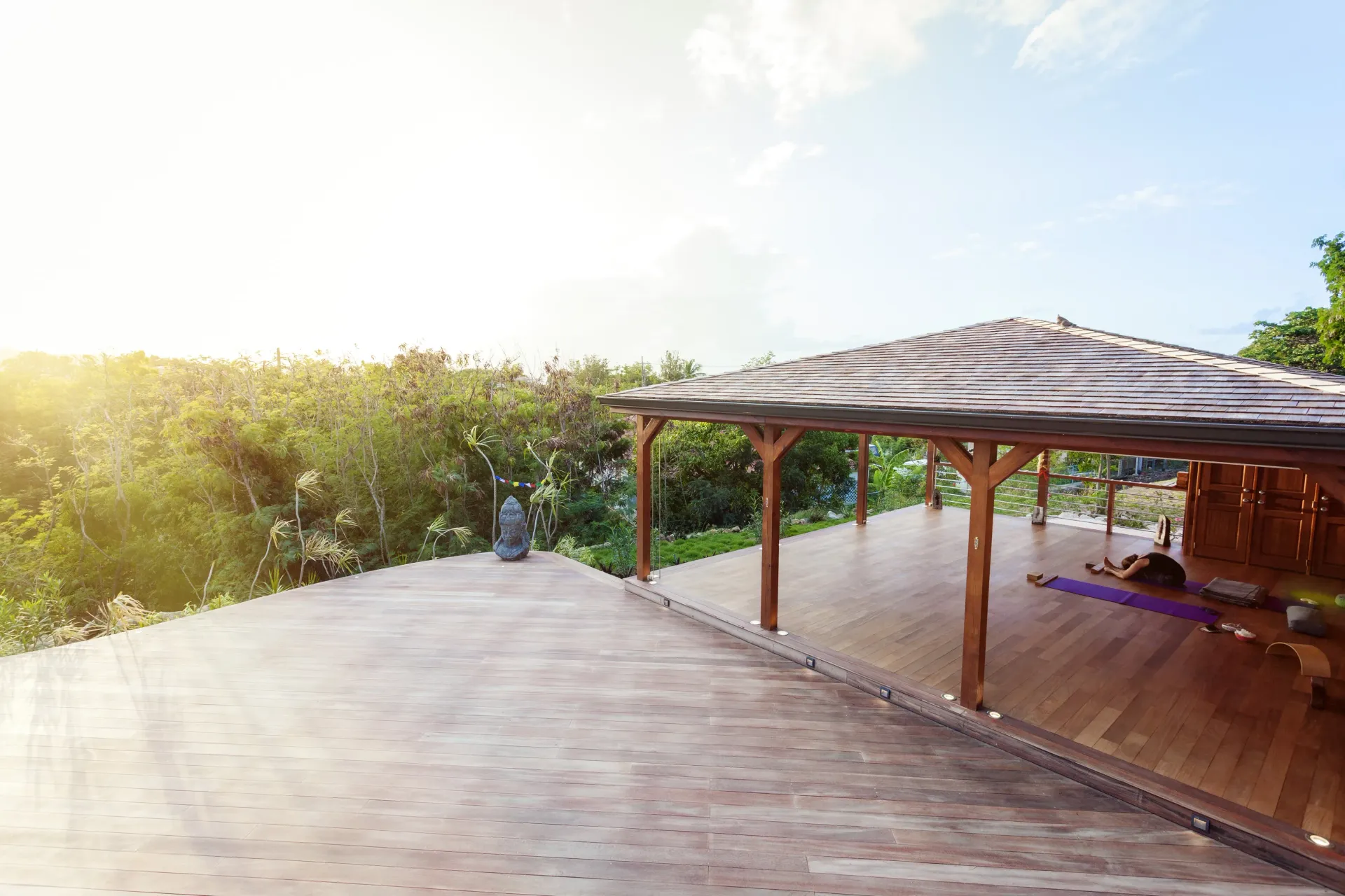 Wooden yoga studio overlooking lush greenery under a bright sky.