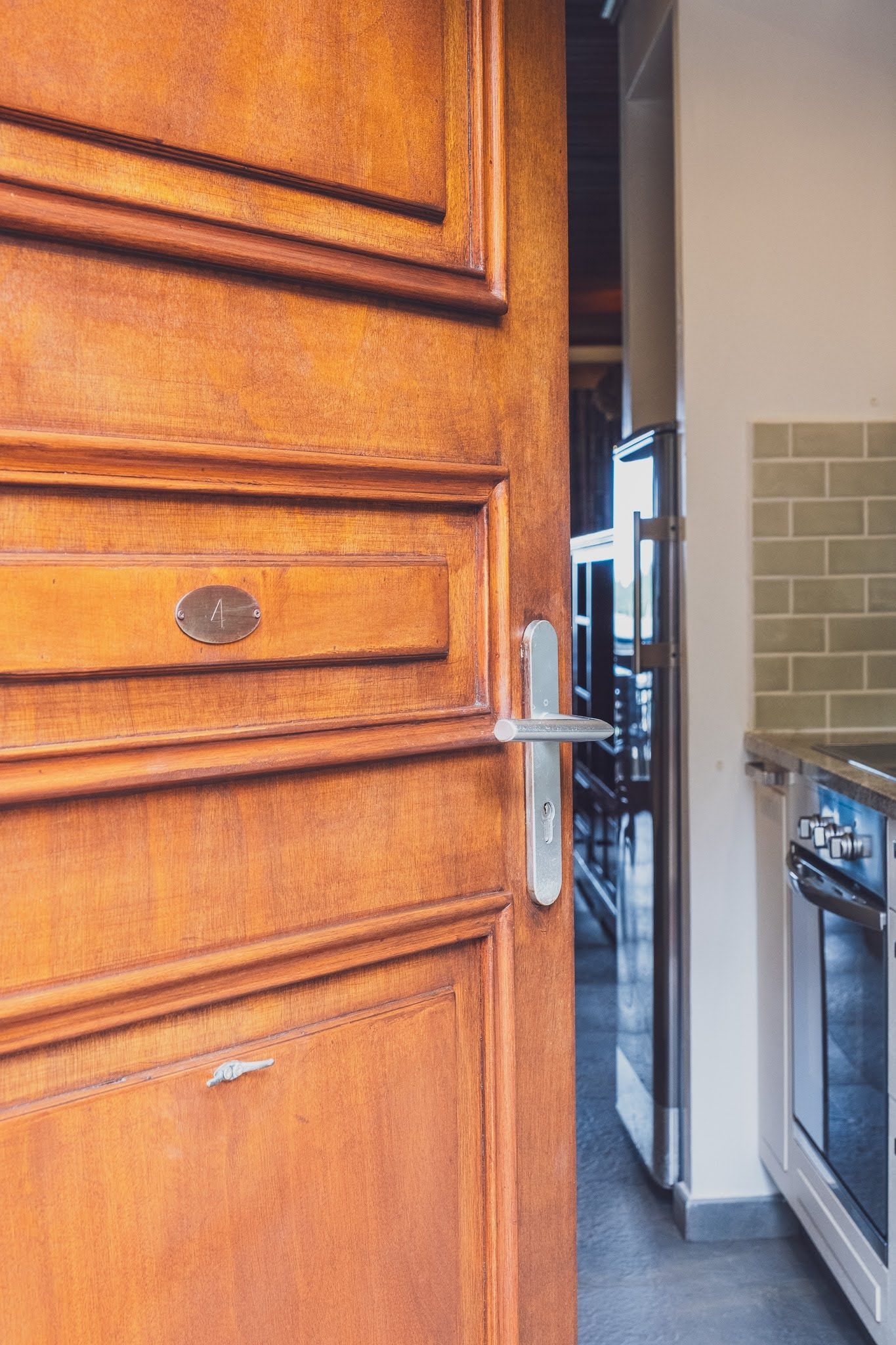 Wooden door partially open, revealing a kitchen with stainless steel appliances and a tiled backsplash.