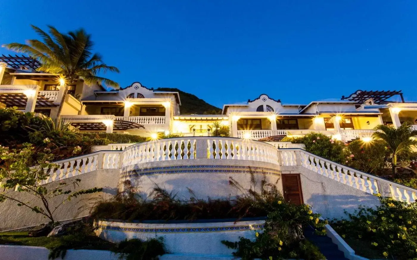 White stucco building with a long staircase at dusk, with a lighted facade.