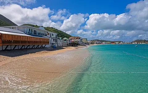 Beach with buildings, turquoise water, and blue sky with clouds.