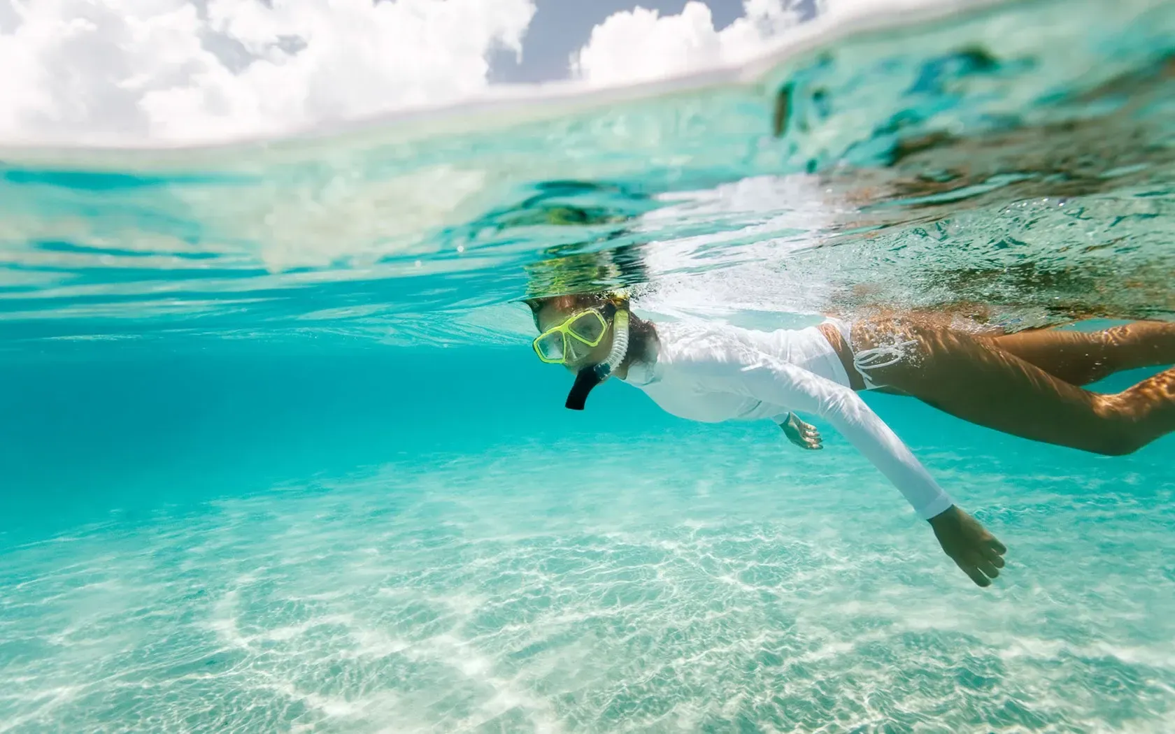Woman snorkeling in clear turquoise water, wearing a white rash guard and mask.