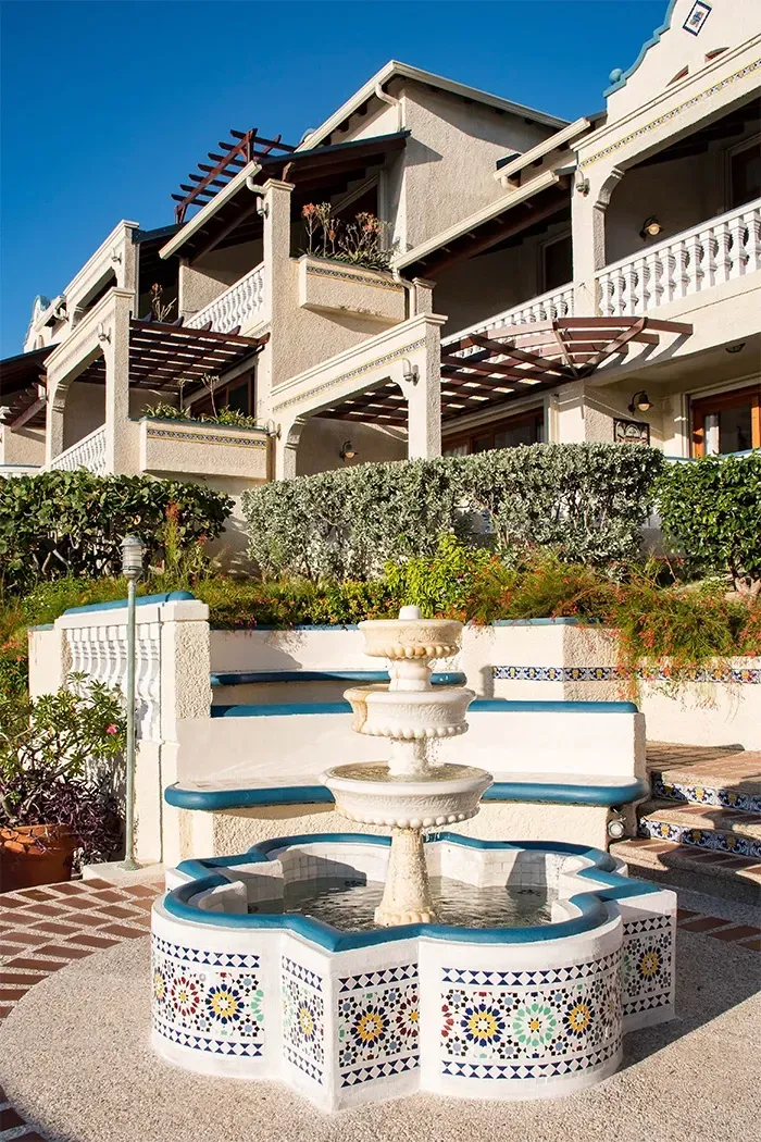 Fountain in front of a multi-story building with balconies and a blue sky.