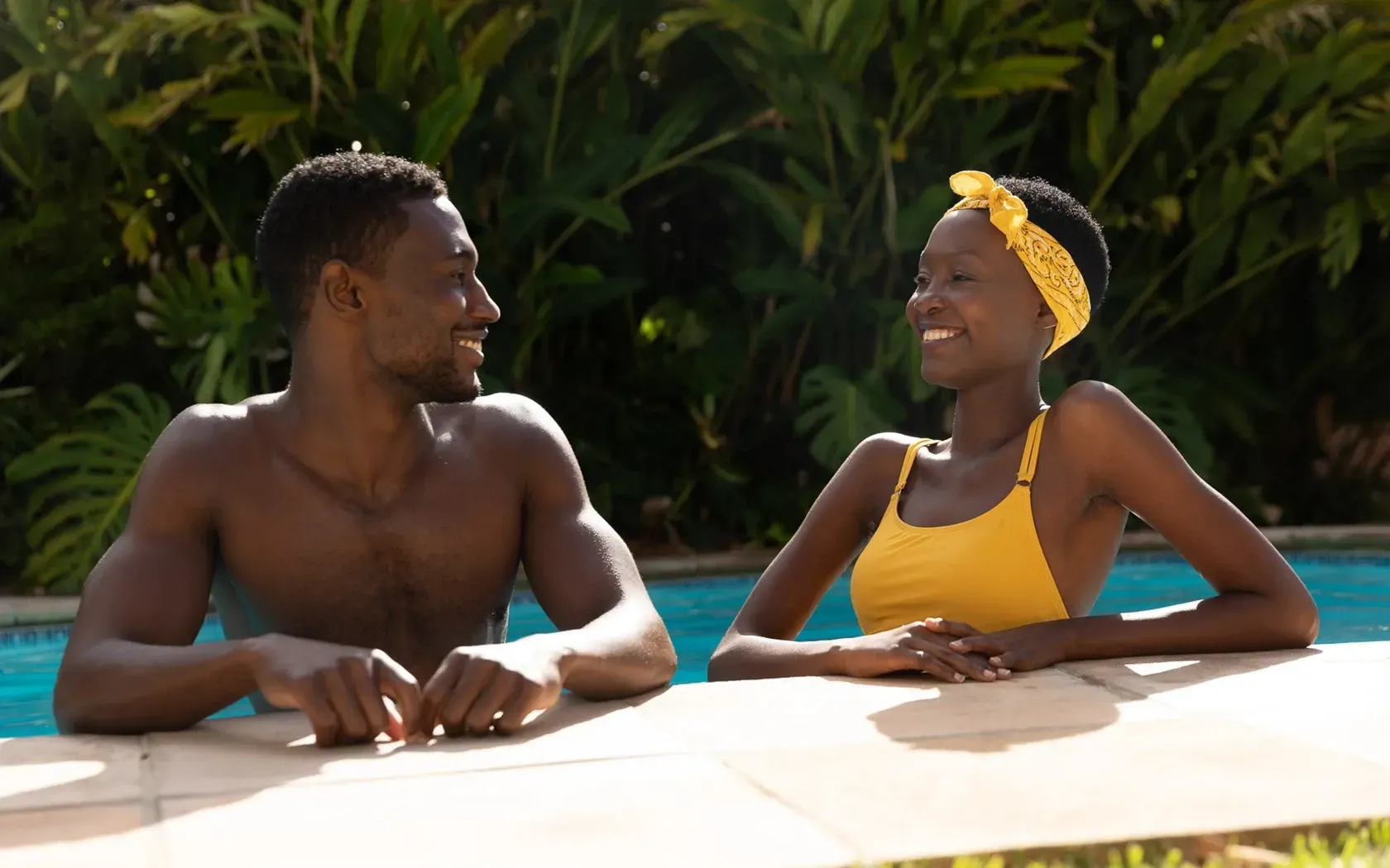 Man and woman smiling at each other in a pool, woman wearing a yellow bathing suit and headband.