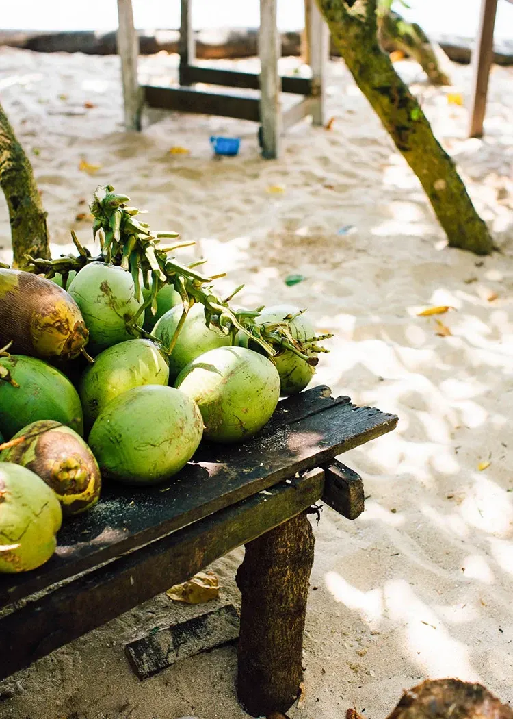 Green coconuts on a rustic wooden table at a sandy beach.