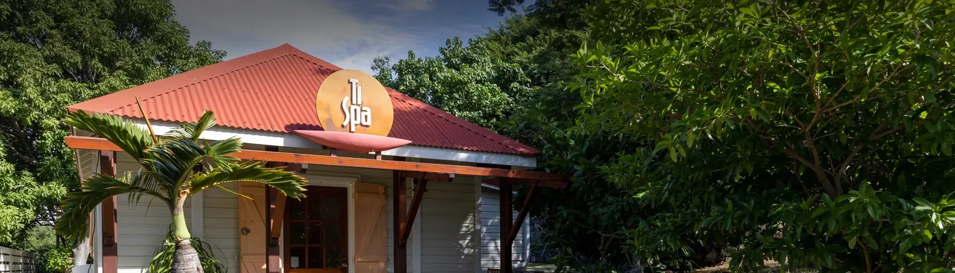 A white building with a red roof and a sign on the roof is surrounded by green trees.
