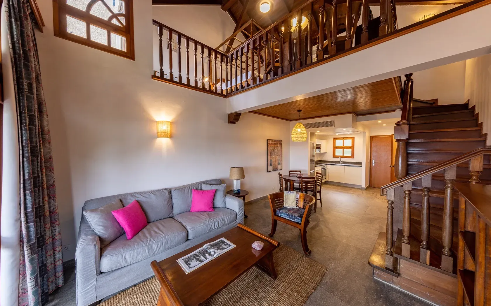 Spacious living area with a loft, sofa, and wooden staircase. Neutral walls, cozy design.