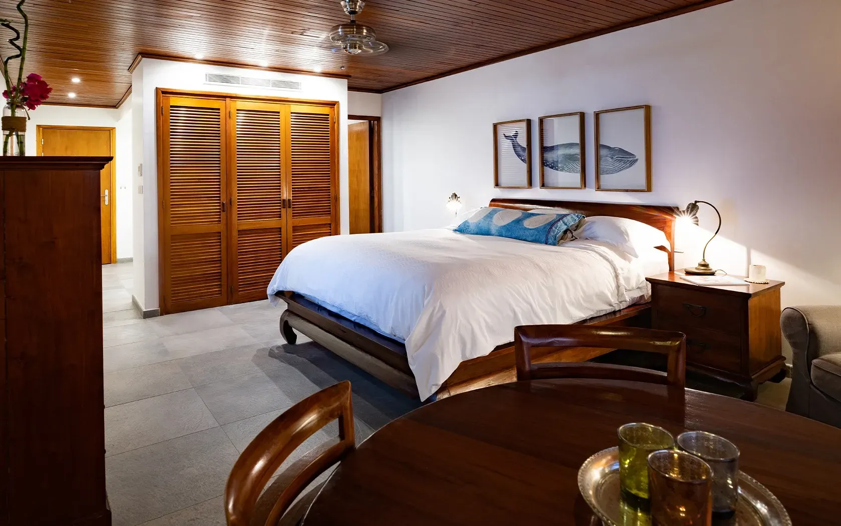 Bedroom with wooden furniture, king-size bed, artwork, and a round table with chairs.