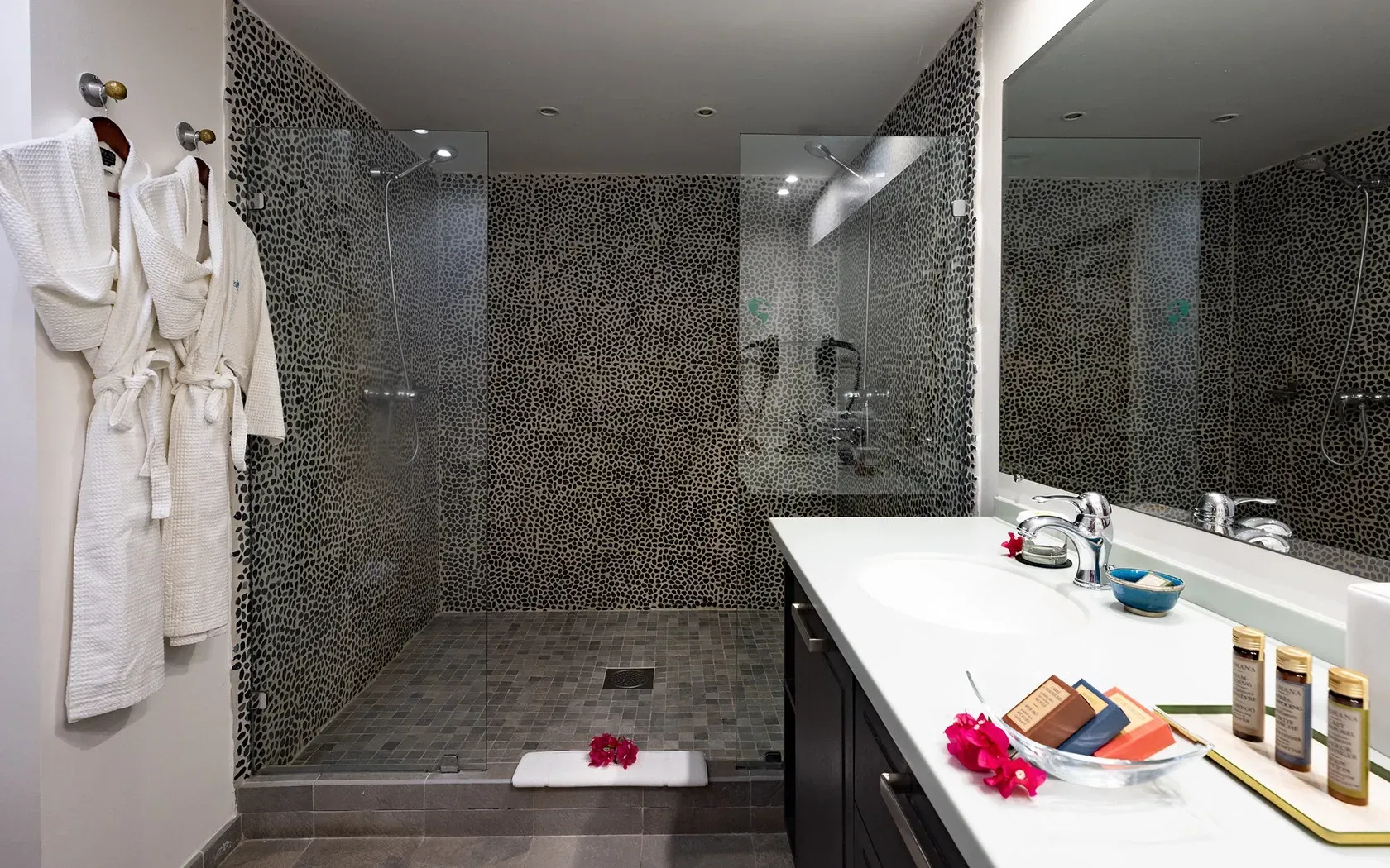 Bathroom with glass shower, robes, vanity, and mosaic tile walls.