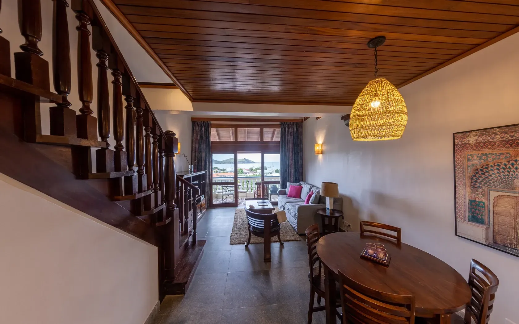 Interior with wooden staircase, dining area, living room, and sea view through a window.