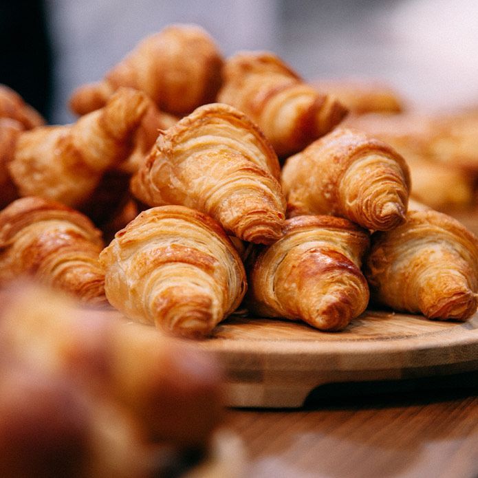Pile of golden-brown croissants on a wooden board, ready to eat.