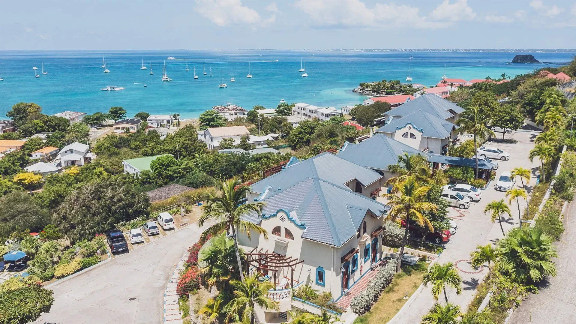 Coastal houses overlooking a bay with sailboats; blue water and sky, tropical setting.