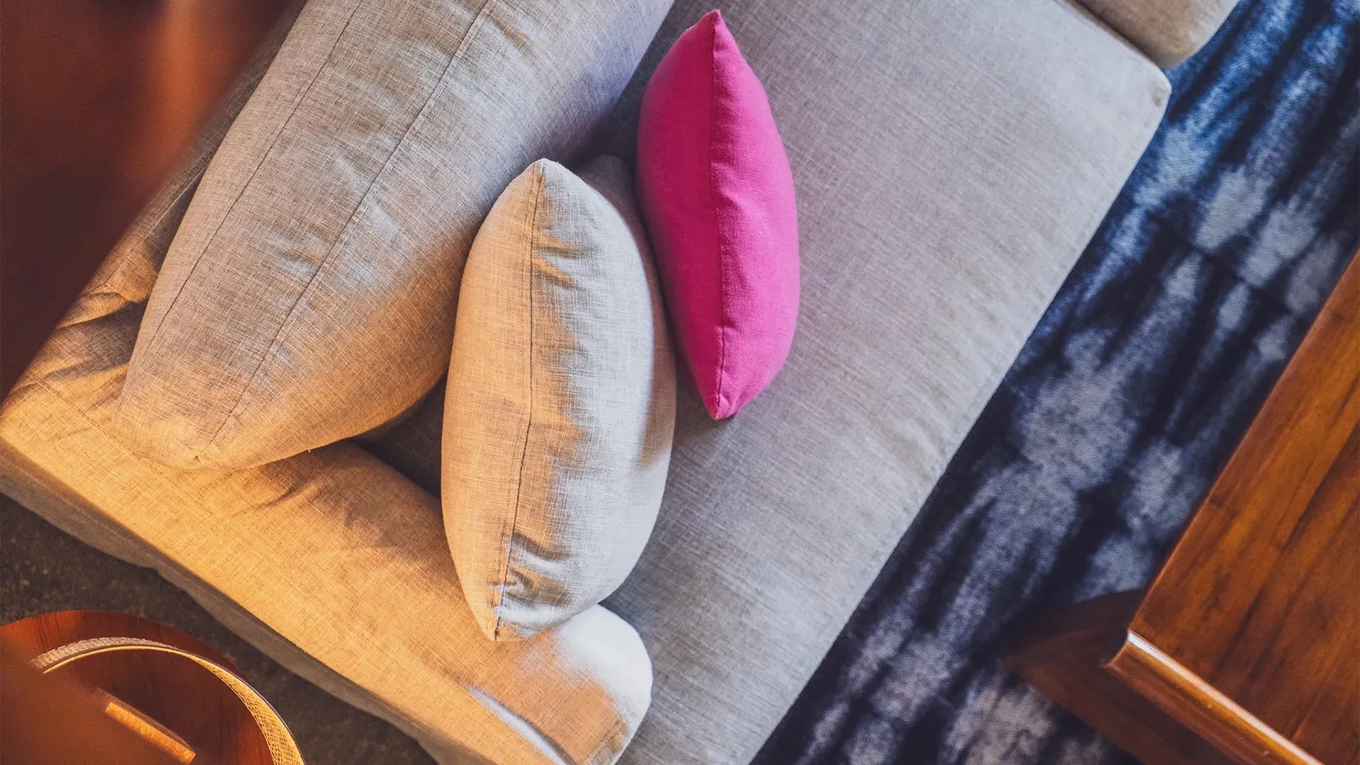 Pillows on a sofa, including white, pink, and gray. Top-down view with patterned fabric.