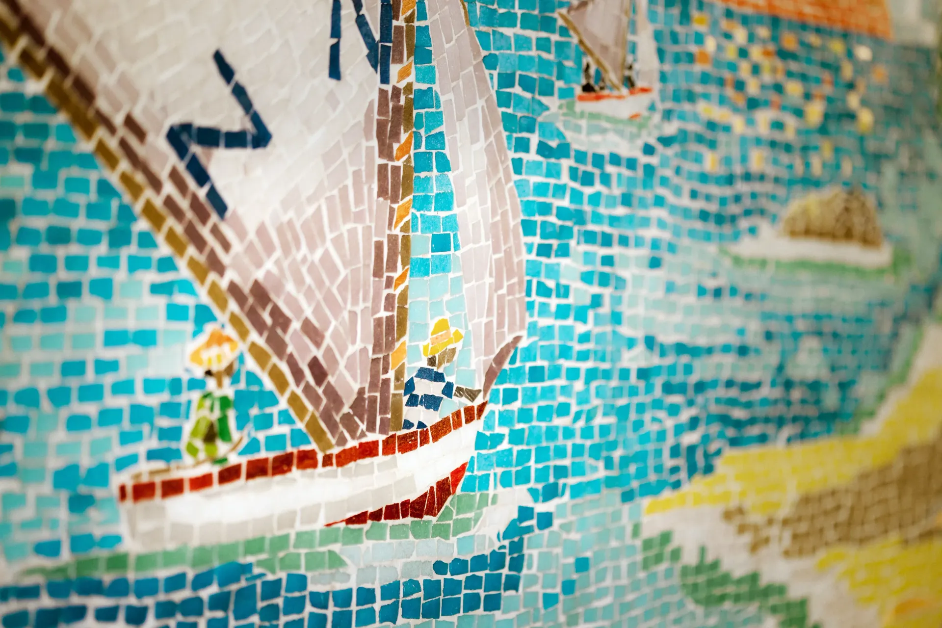 Mosaic art of a sailboat with two people on it, sailing on a turquoise sea.