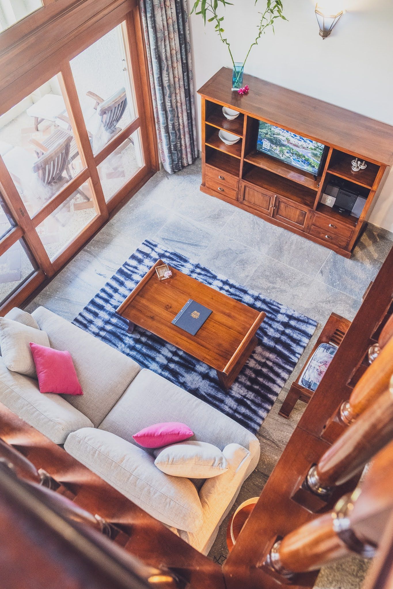 Living room viewed from above, with sofa, rug, wooden furniture, and large windows.