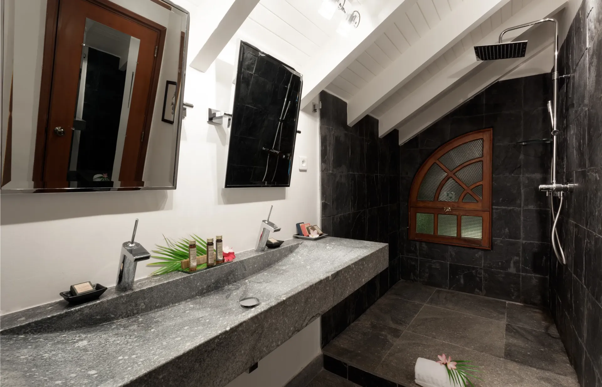 Bathroom with gray granite countertop, black tiled shower, wooden accents, and arched window.