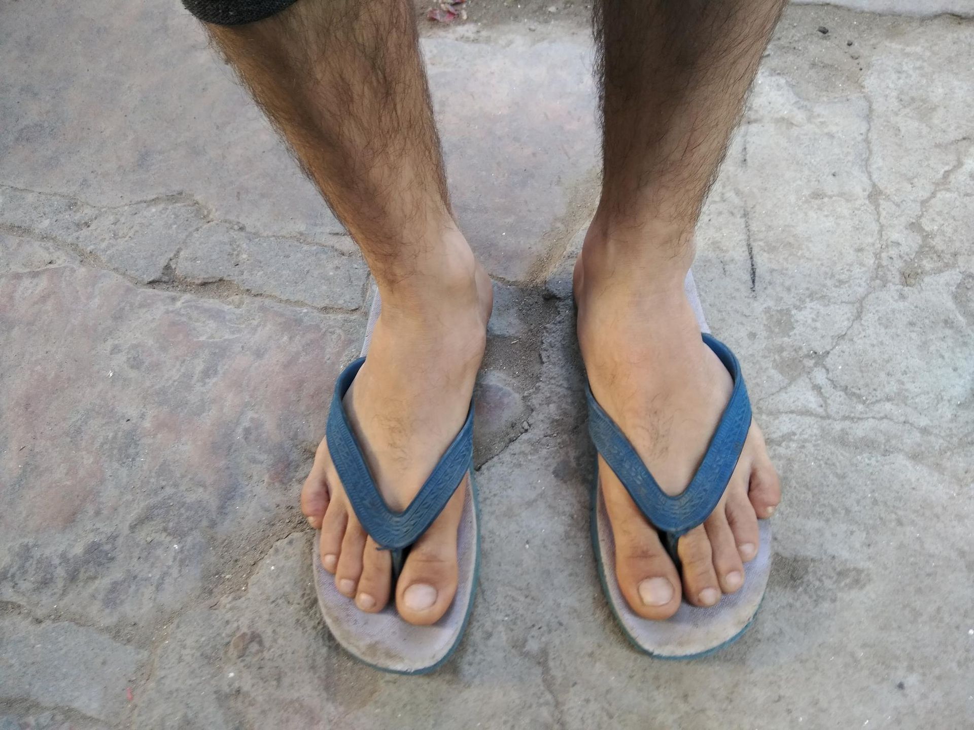 A man wearing flip flops is standing on a concrete surface.