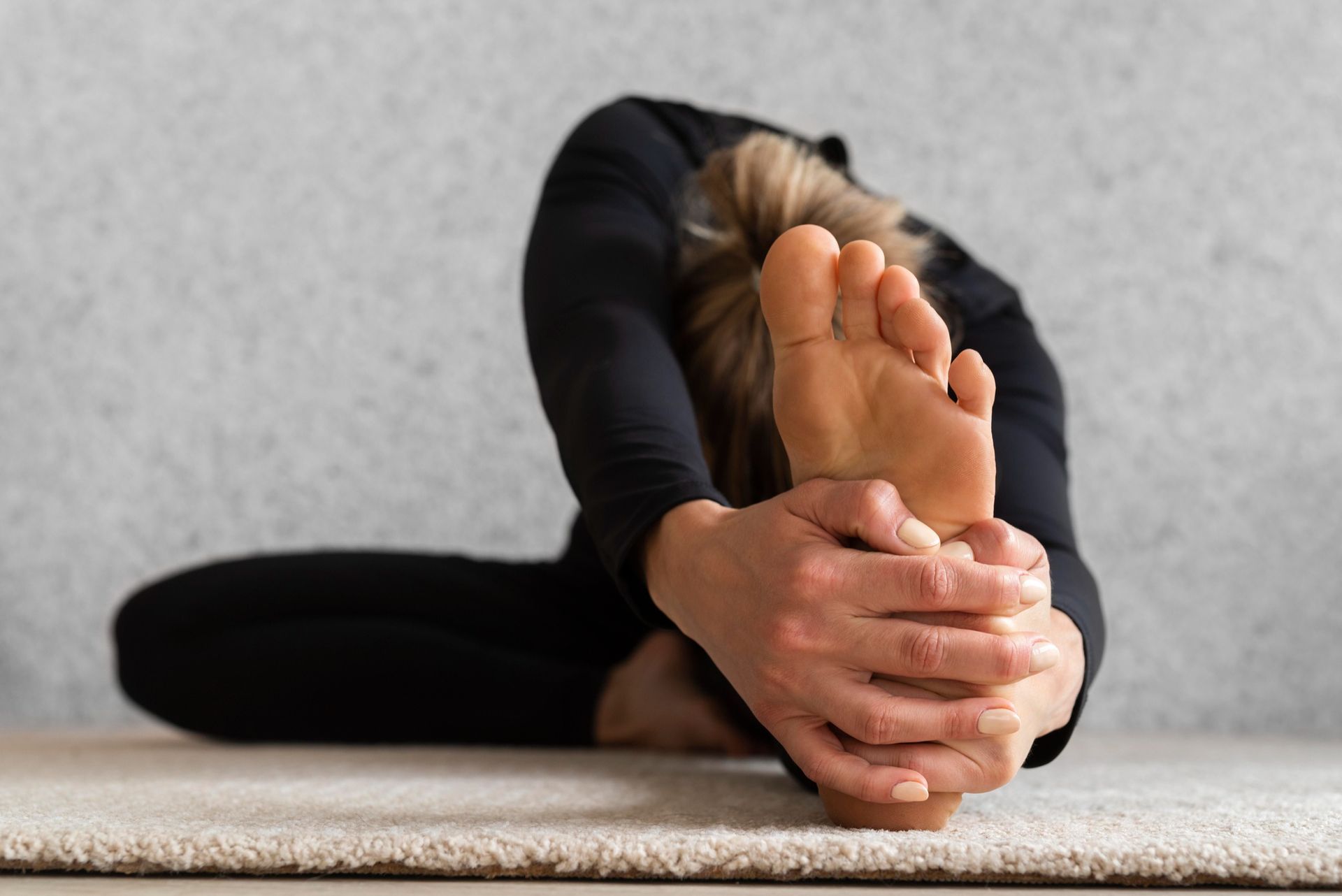 A woman is stretching her legs on a yoga mat.