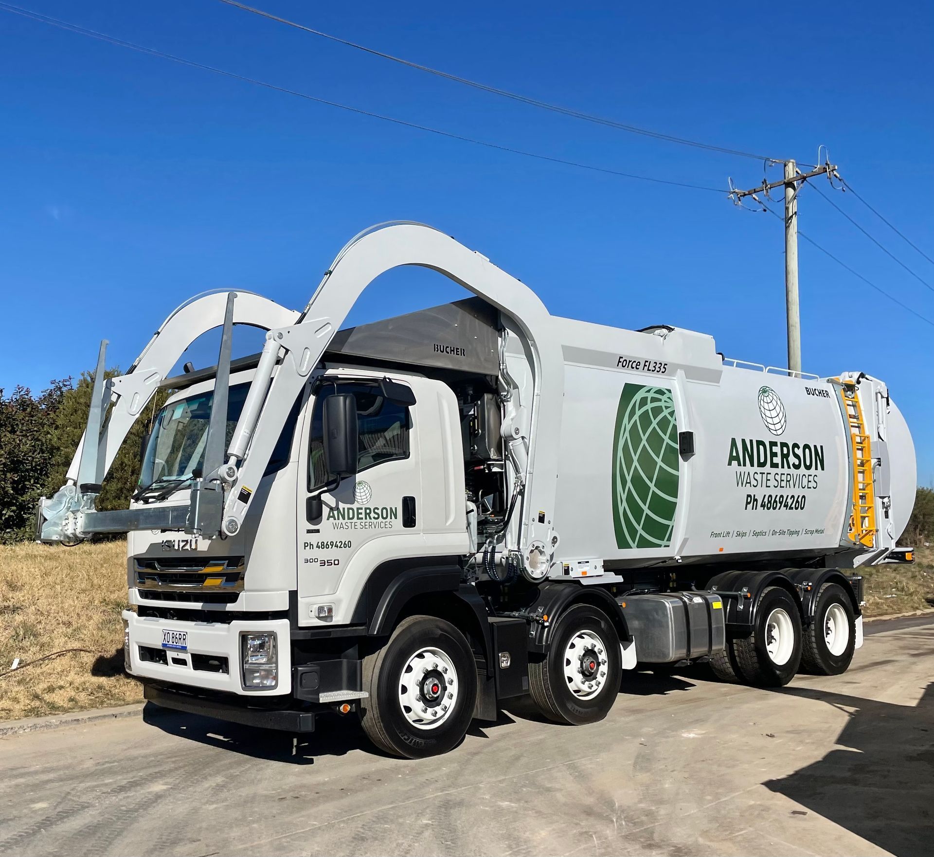 A white Anderson waste collection truck parked on a paved road under a blue sky.
