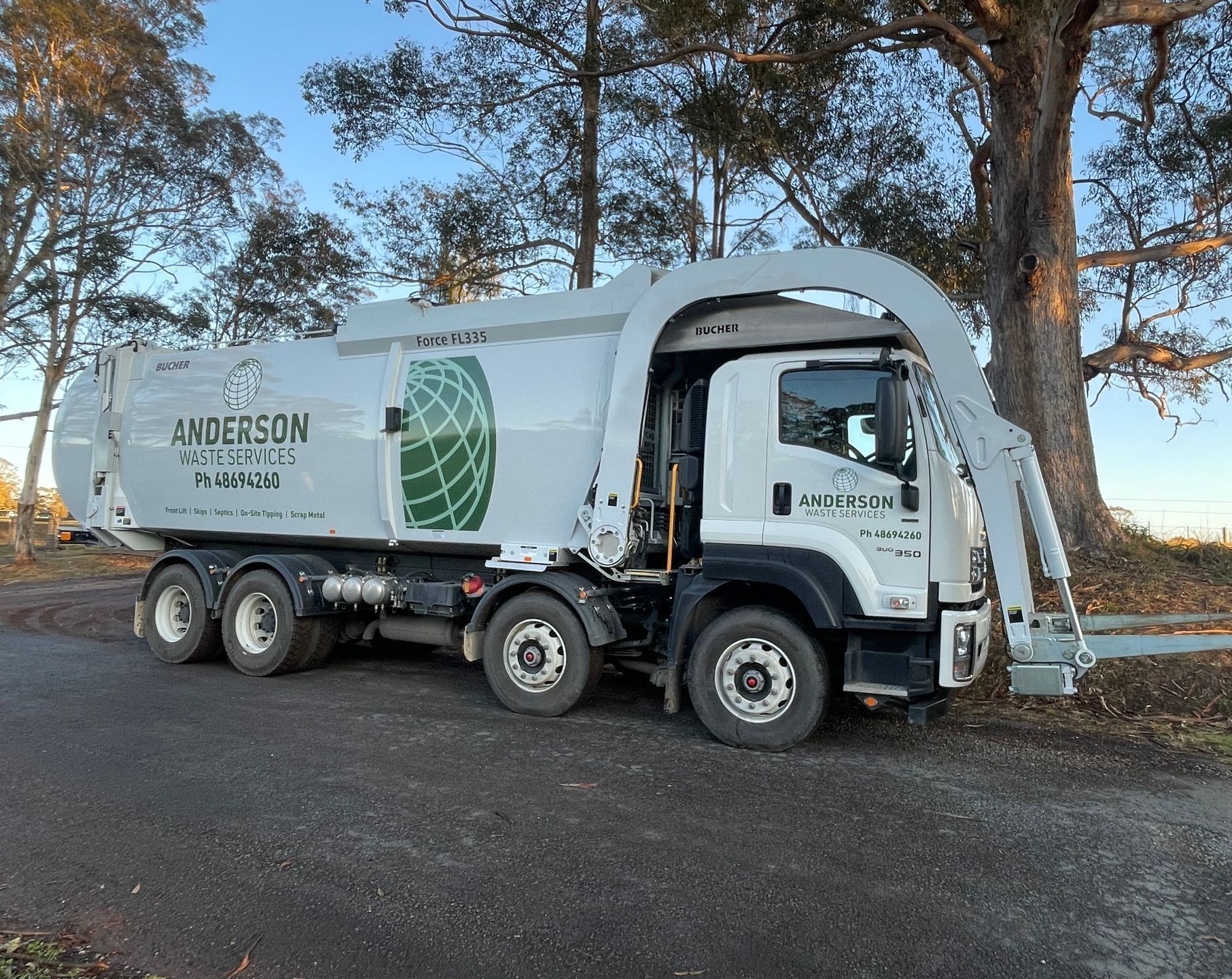 White garbage truck parked outdoors with a large lifting arm, Anderson Sanitary logo visible on side.