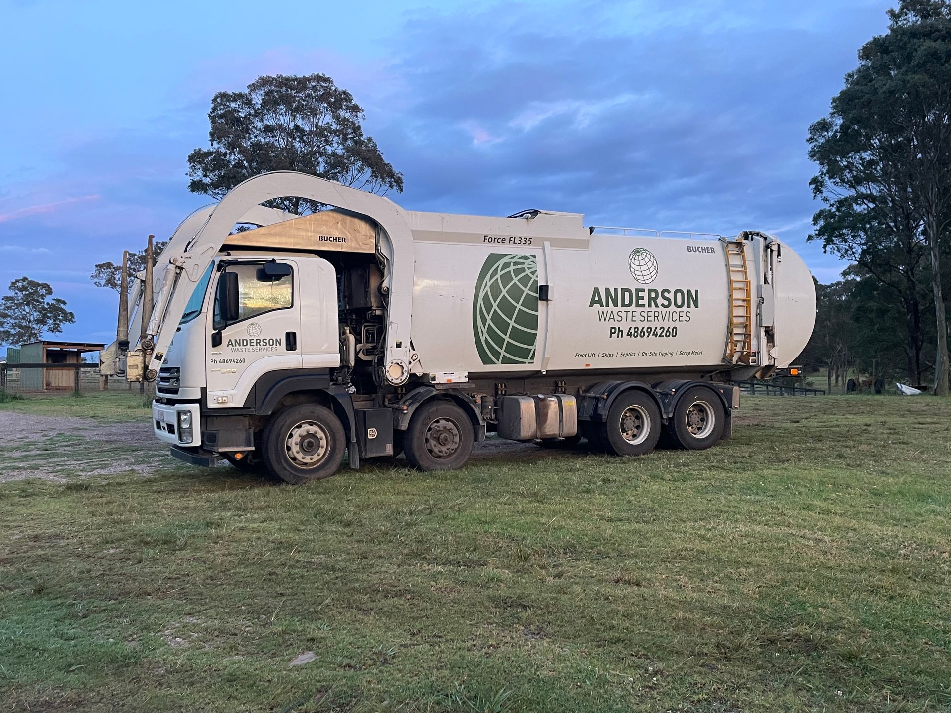 White garbage truck parked on a grassy area, 