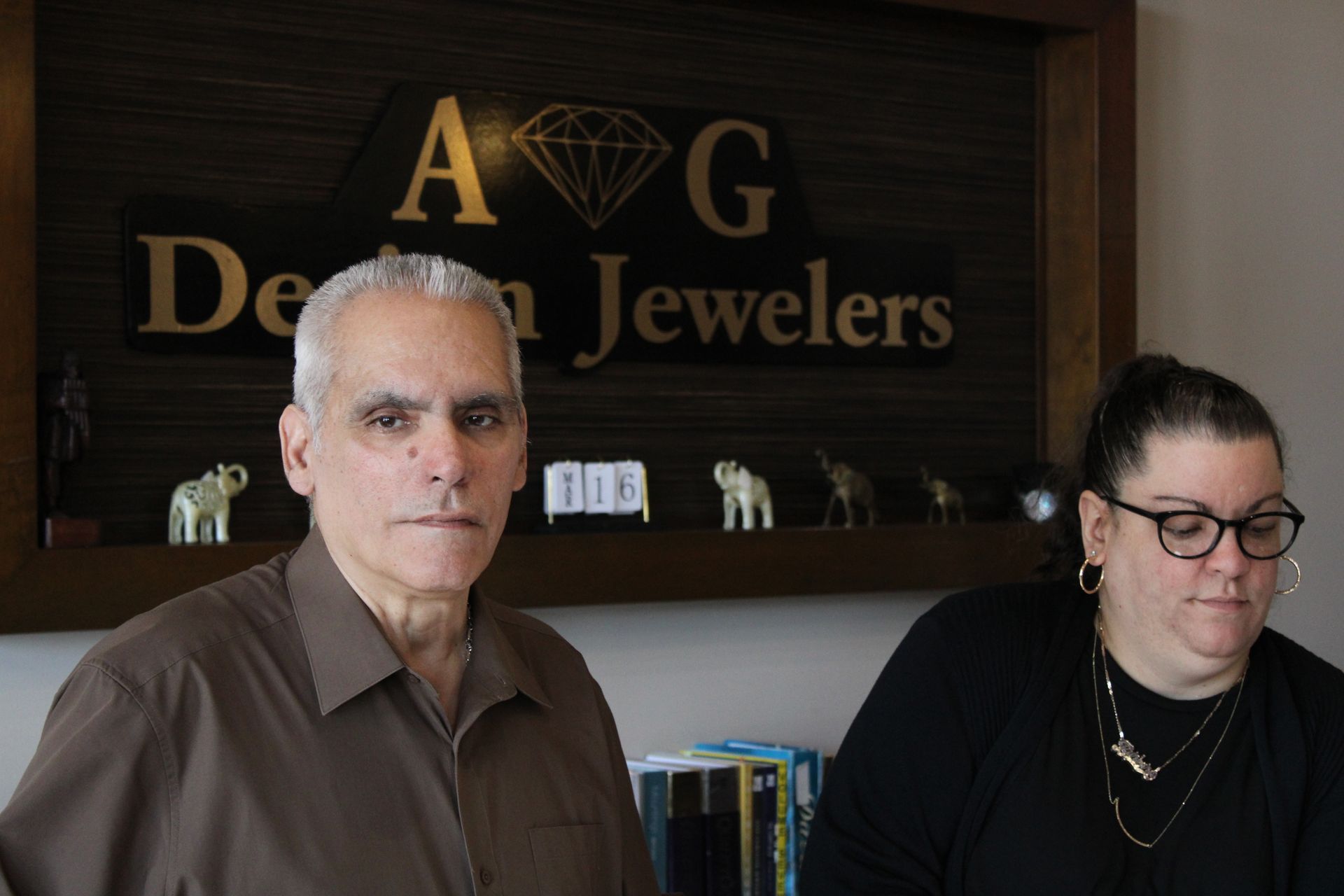 a man and a woman are standing in front of a sign that says a & g design jewelers .