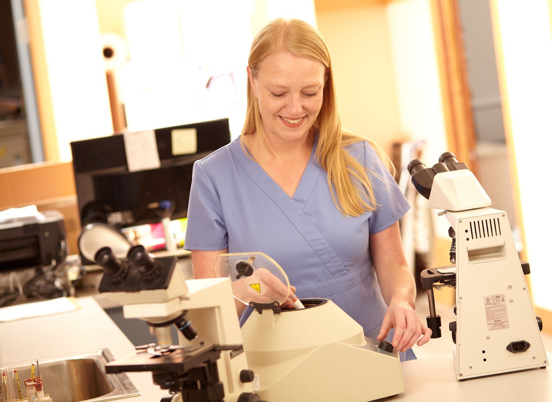 A woman is standing in front of a microscope in a lab.