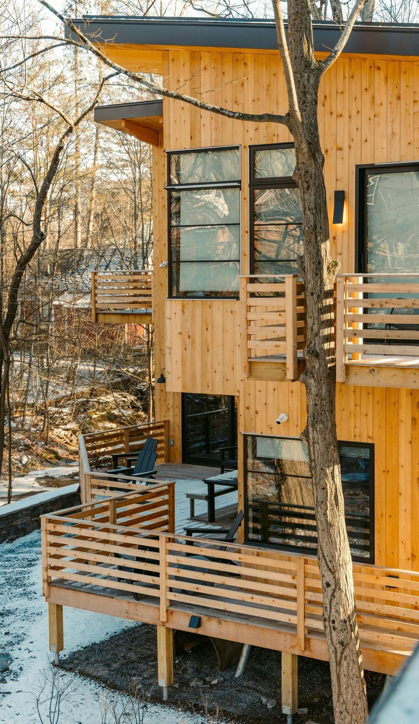 A wooden house with a deck in the snow surrounded by trees.