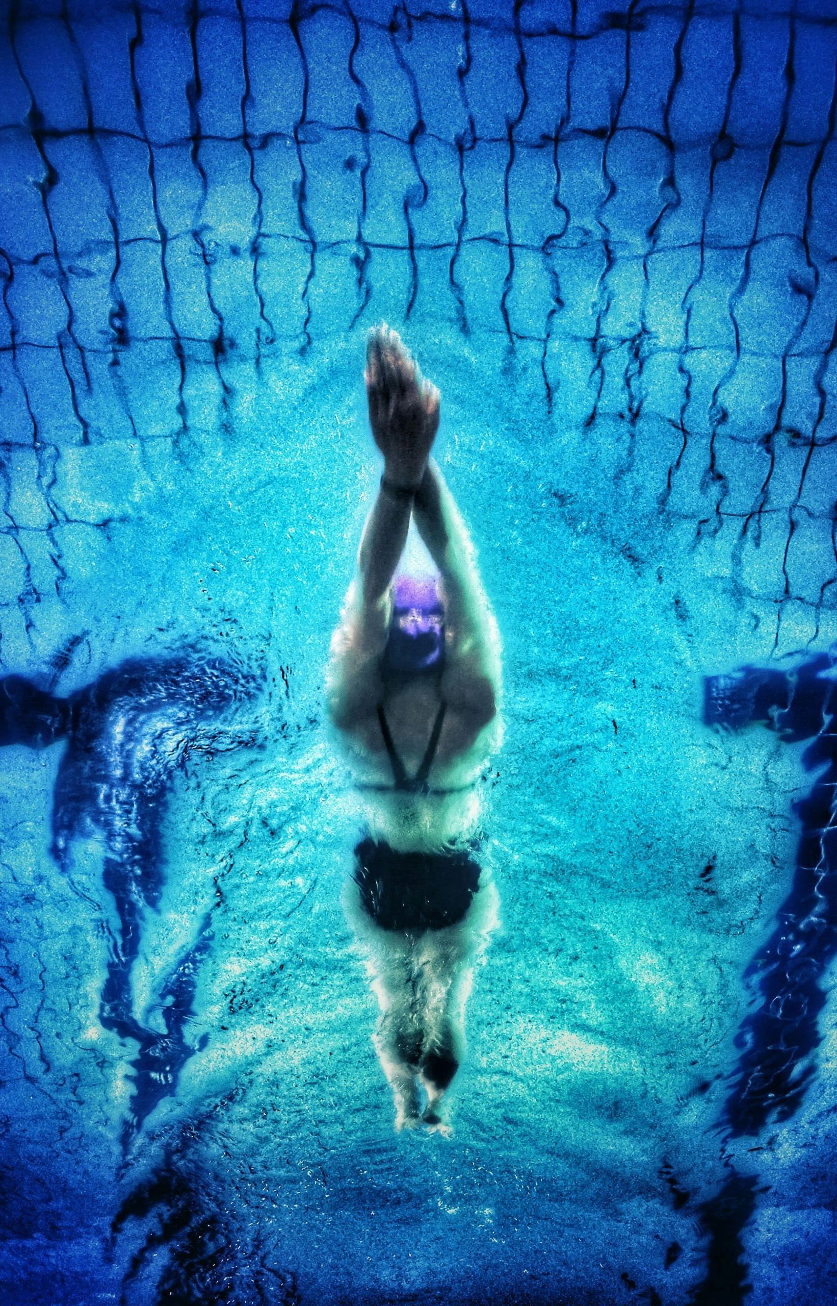 A woman is swimming in a pool with her arms outstretched.