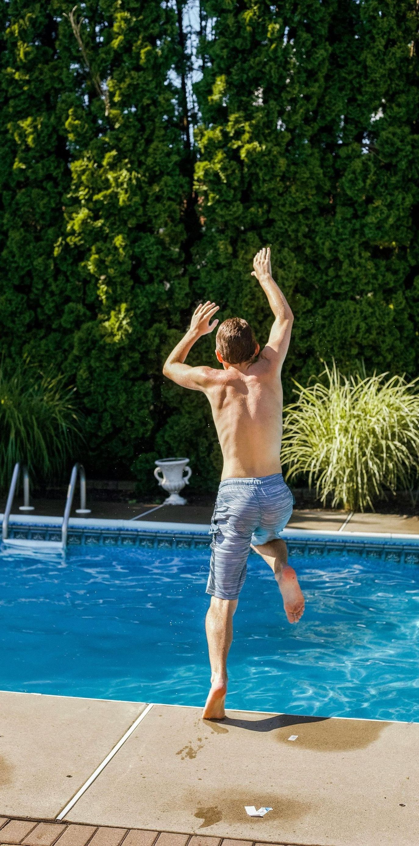 A shirtless man is jumping into a swimming pool.