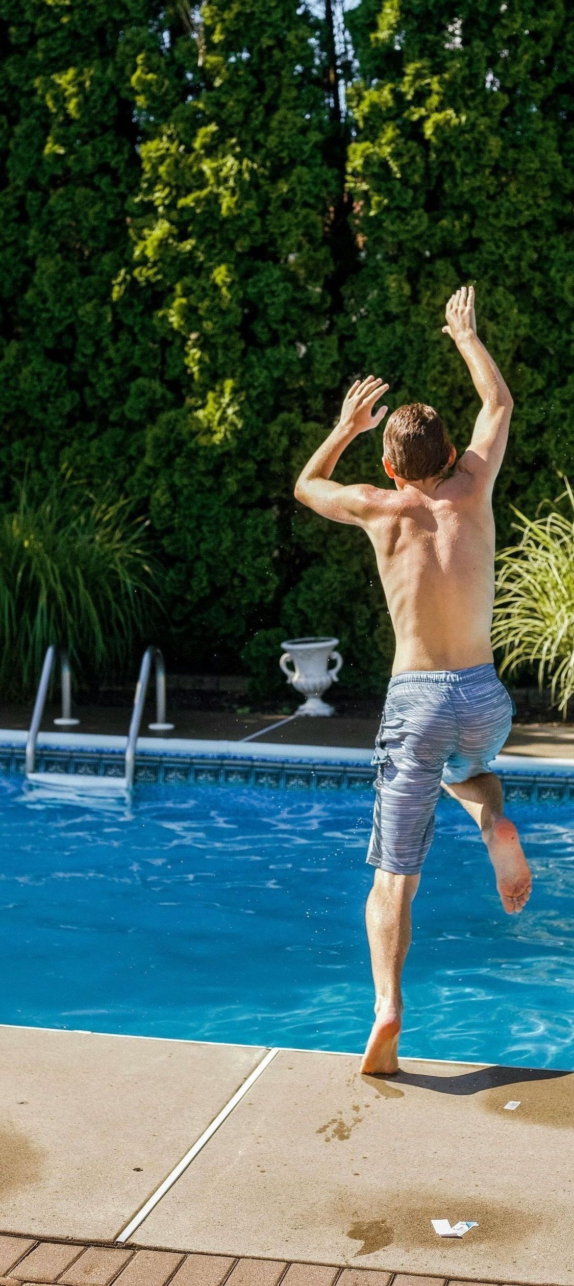 A shirtless man is jumping into a swimming pool.