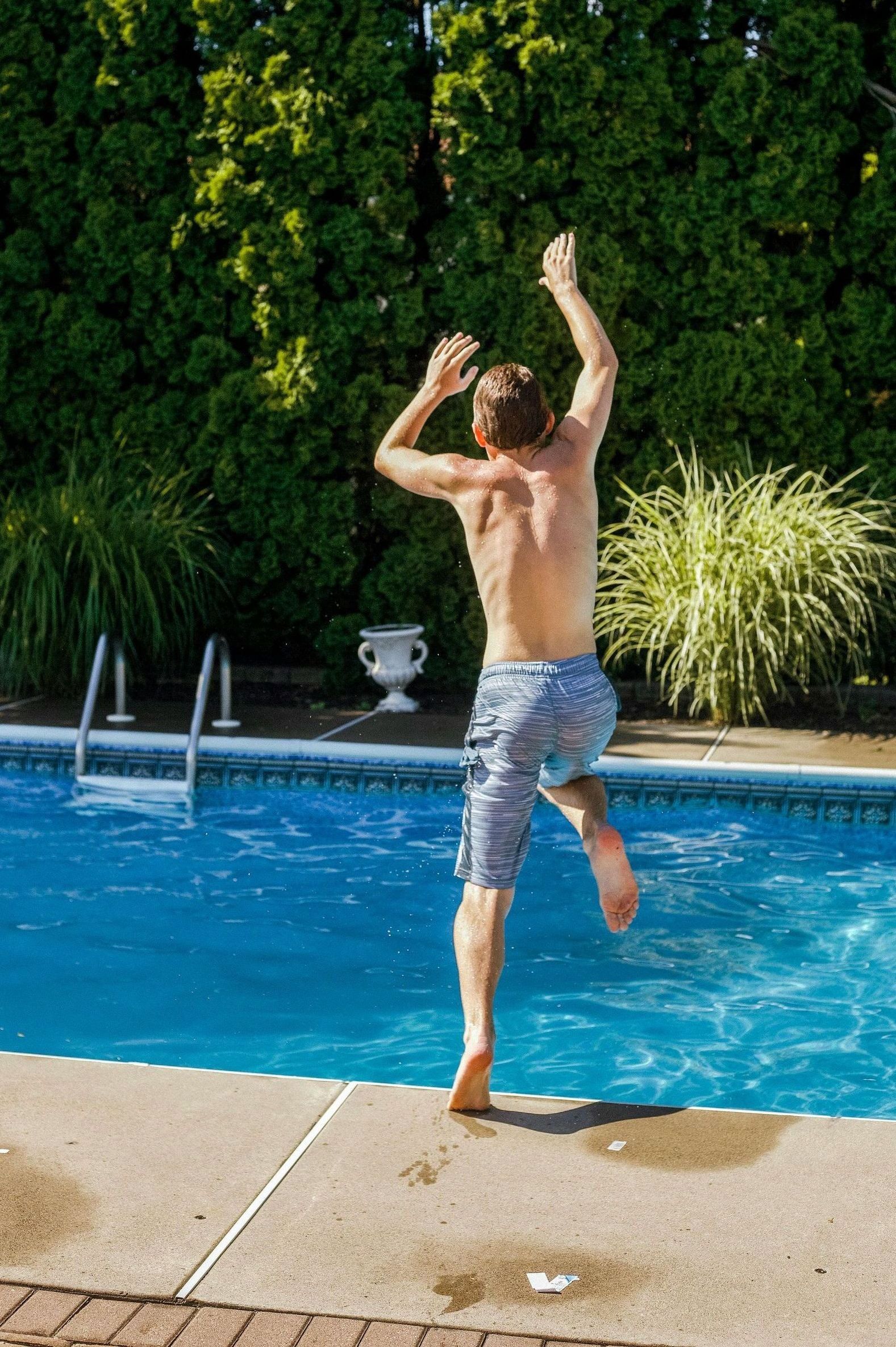 A shirtless man is jumping into a swimming pool.